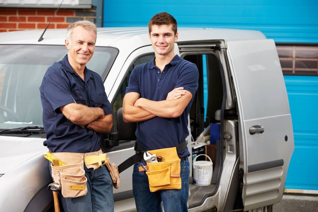 plumbers in a uniform standing in front of a vehicle.