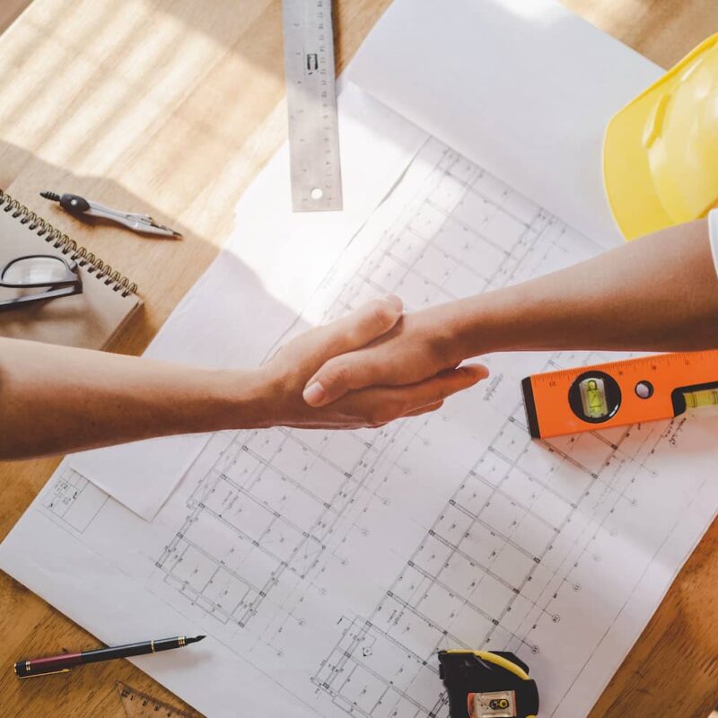 Digital Marketing Agency for Contractors 2 Two contractors shaking hands over blueprints and tools โ symbolizing trust, partnership, and success with a digital marketing agency for contractors.