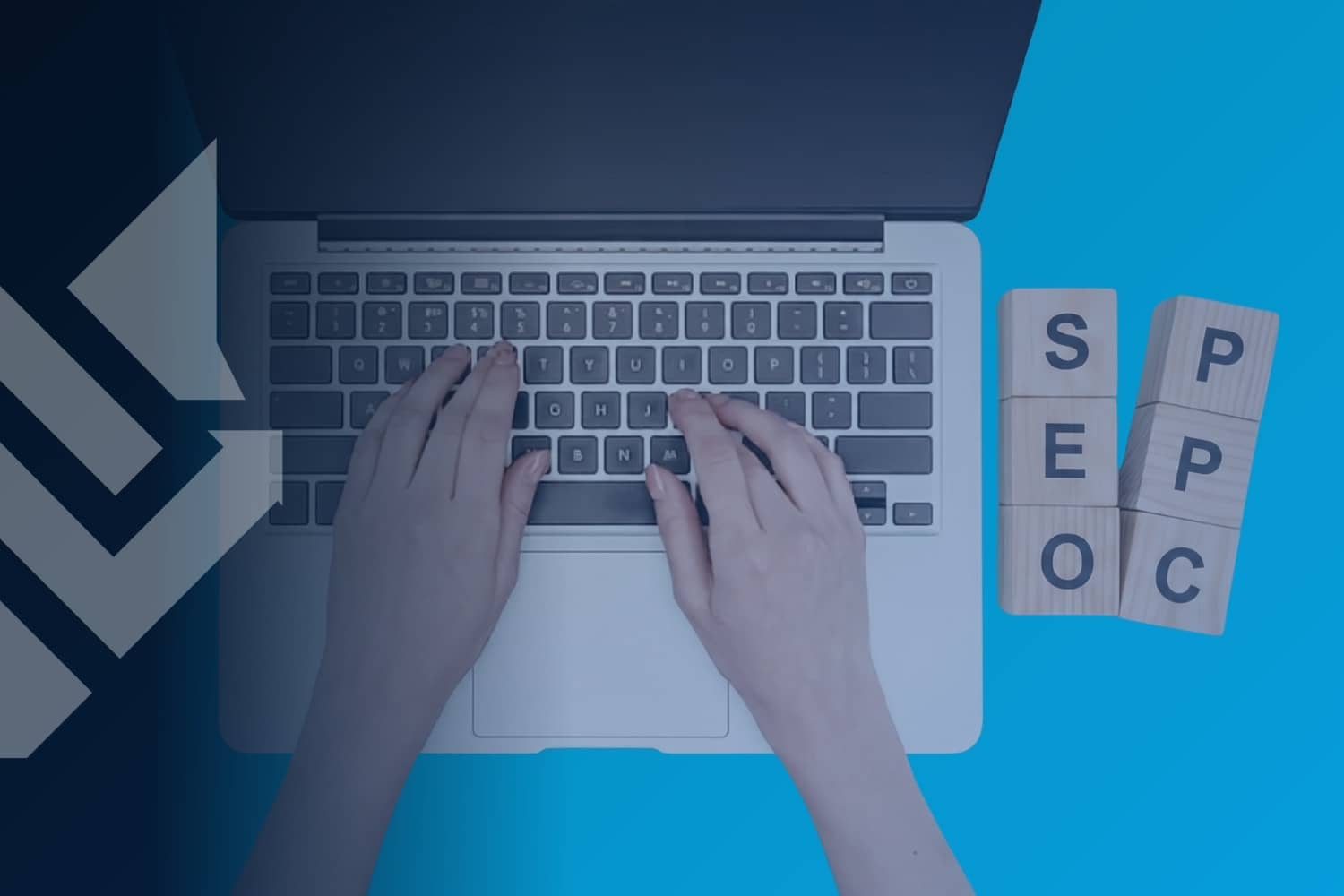 An overhead view of a person typing on a laptop with two stacks of wooden toy blocks on the right side of the desk, one spelling out SEO and the other spelling out PPC, illustrating the comparison of SEO vs PPC.