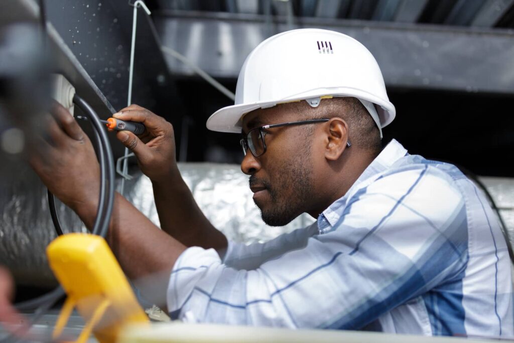 Electrician wearing a white hard hat and glasses working on electrical wiring—ideal image for a digital marketing agency for electricians.